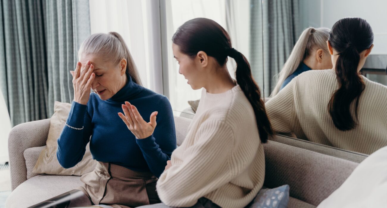 An adult daughter and her elderly mother sharing a tender, supportive conversation on the couch at home