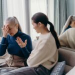 An adult daughter and her elderly mother sharing a tender, supportive conversation on the couch at home