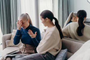An adult daughter and her elderly mother sharing a tender, supportive conversation on the couch at home