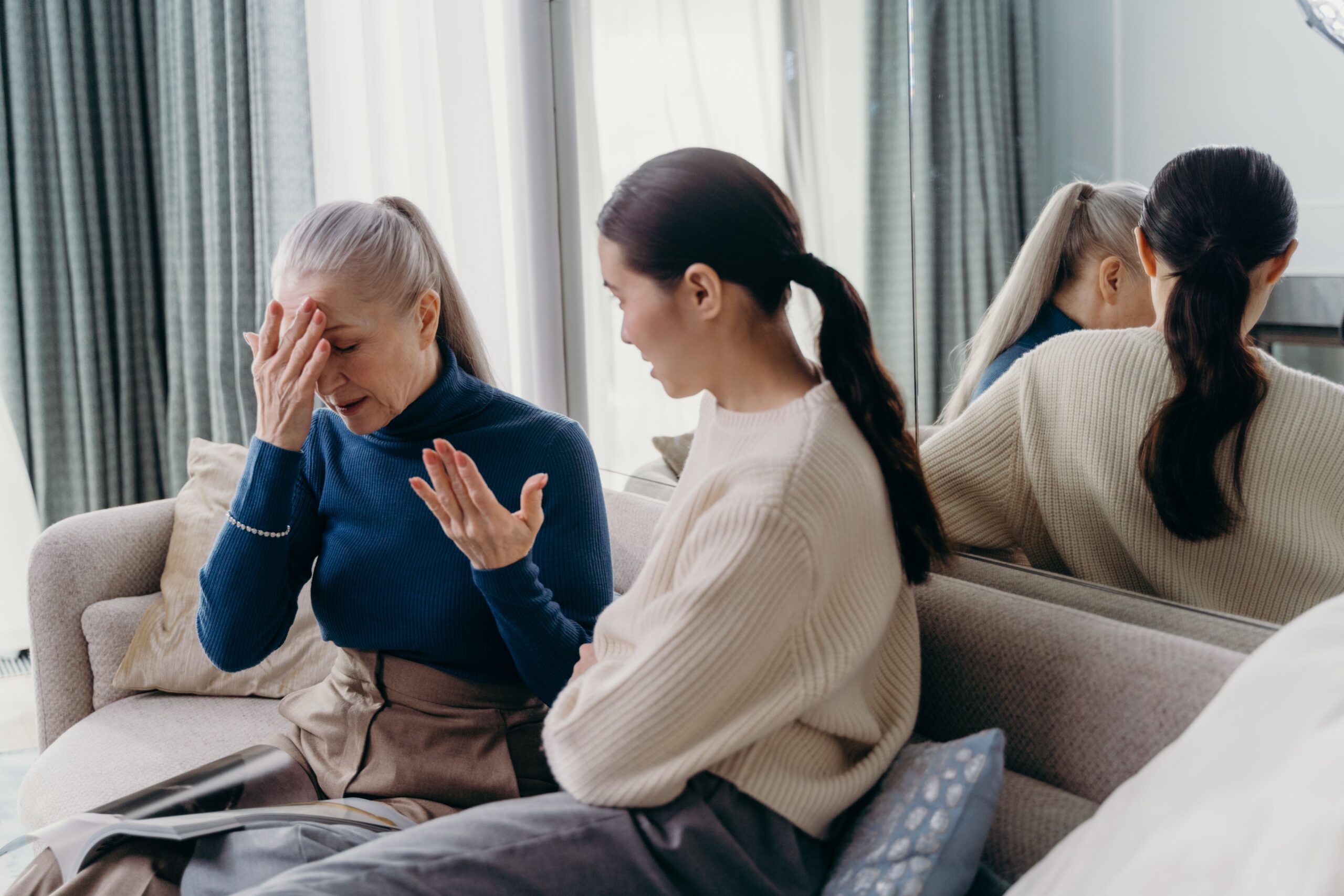 An adult daughter and her elderly mother sharing a tender, supportive conversation on the couch at home