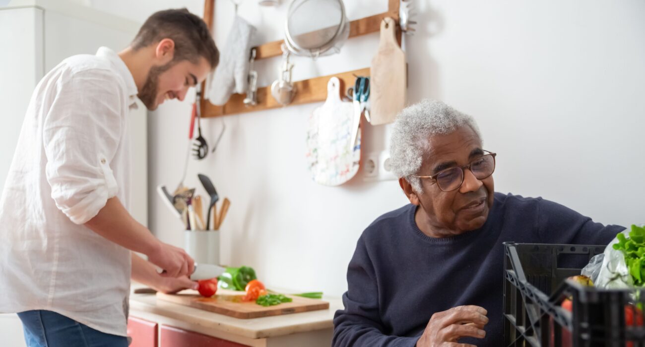 A caregiver and senior man preparing a meal together in the kitchen, an example of the companionship and household support home caregivers provide