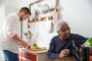 A caregiver and senior man preparing a meal together in the kitchen, an example of the companionship and household support home caregivers provide